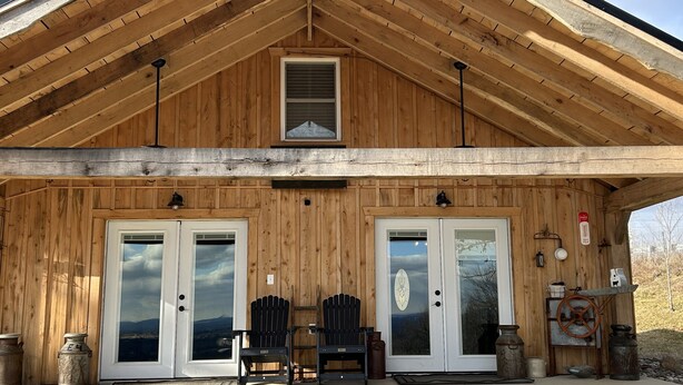 A wooden cabin with a gabled roof, two front doors with glass panels, and a small porch area with two Adirondack chairs. - Charming Cabin - Wake up to the Epic Views, Stay for the Convenience (Carlisle)