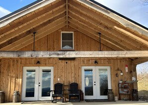Eine Holzhütte mit Satteldach, zwei Eingangstüren mit Glasfeldern und einer kleinen Veranda mit zwei Adirondack-Stühlen.
