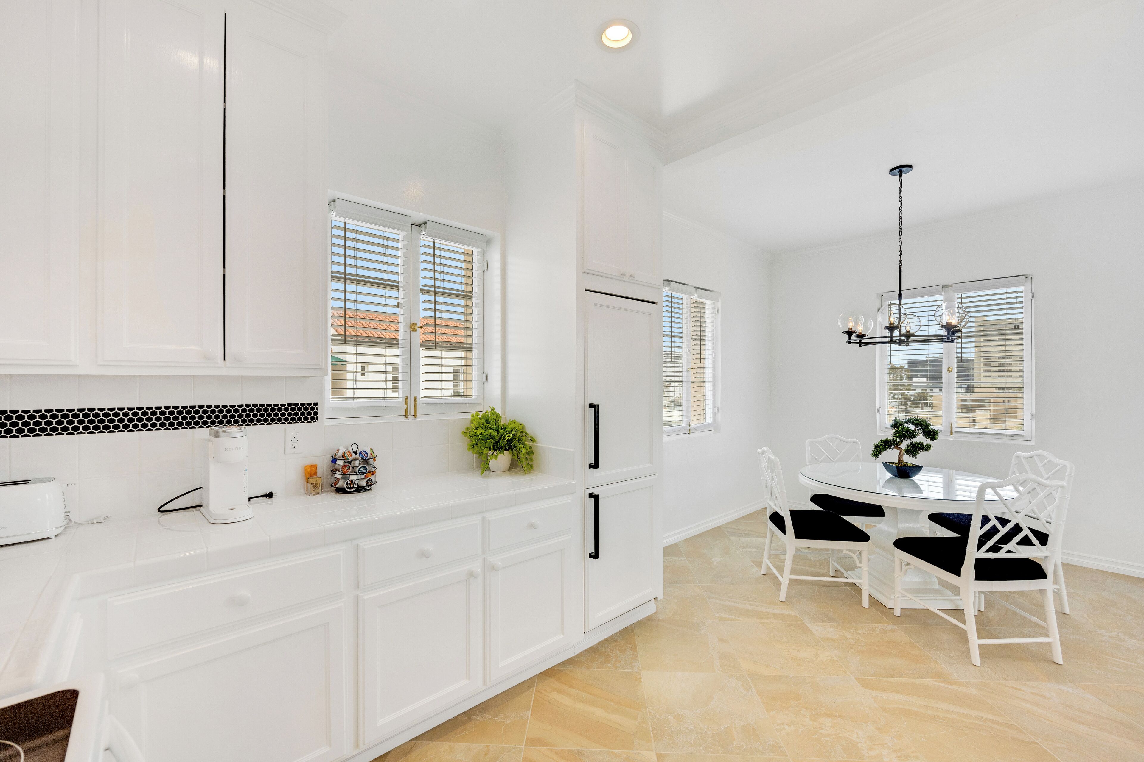 A modern kitchen with white cabinetry, a dining area with a round table and chairs, and a chandelier.