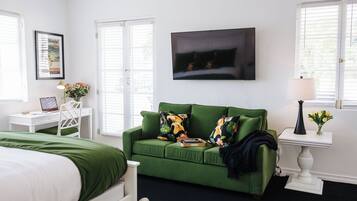 A room with a green sofa, a white desk, a bed, and a TV on the wall.