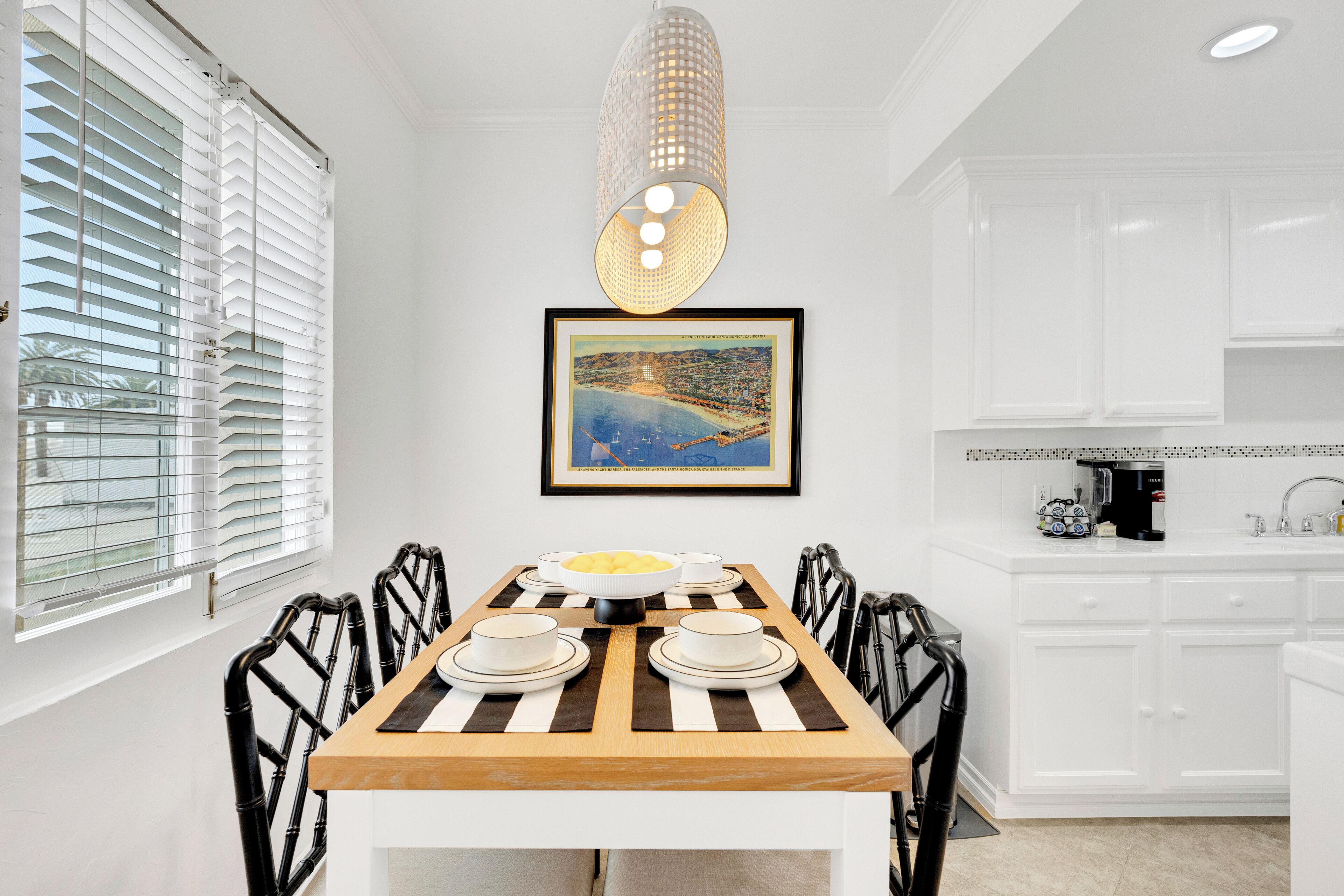 A dining area with a wooden table set for four, white cabinets, and a framed picture on the wall.