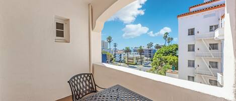A balcony with a table and chair, overlooking a residential area with palm trees and buildings.