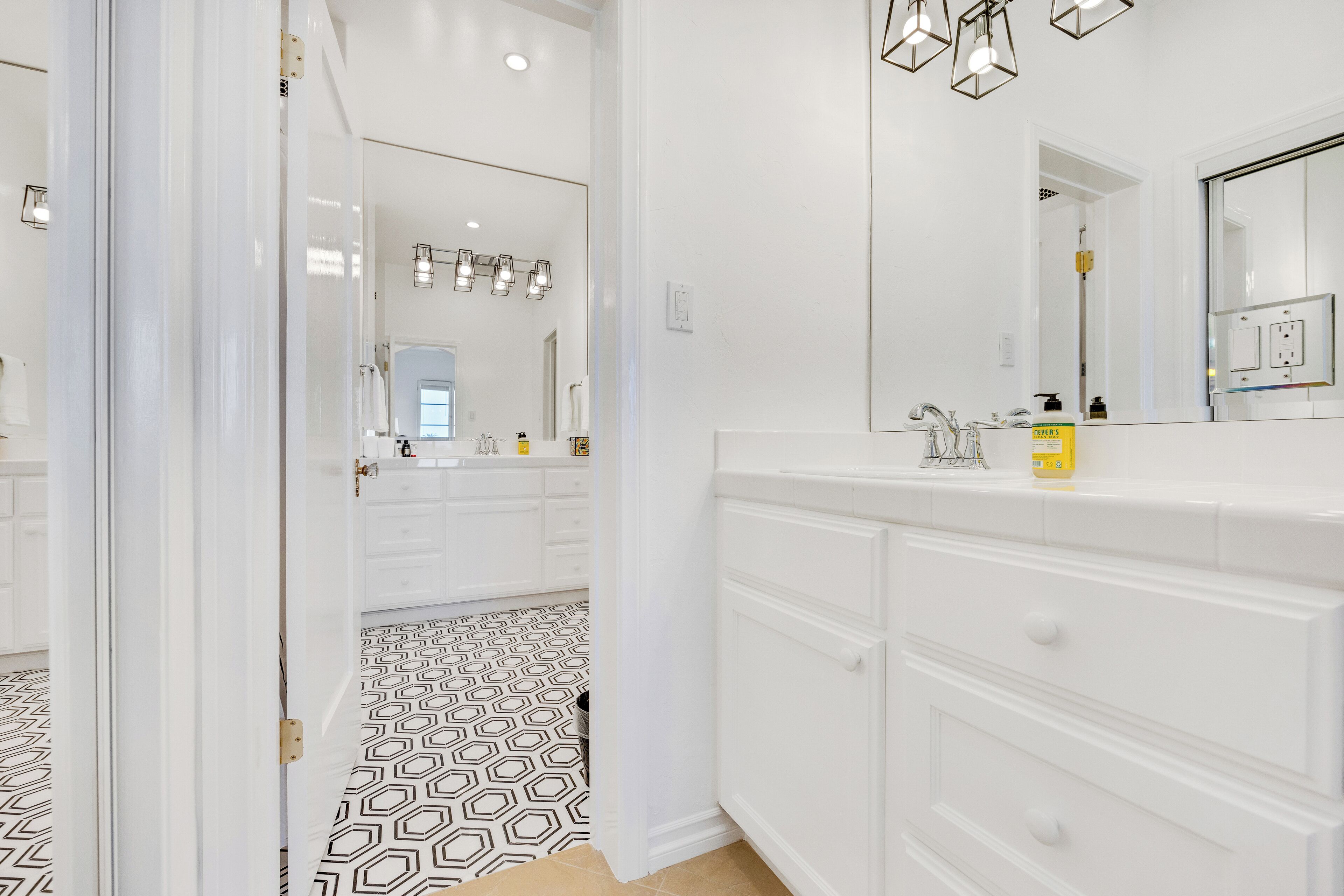 A modern bathroom with a large mirror, white cabinetry, and a patterned floor.