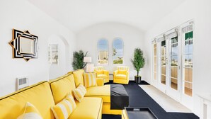 Un salon moderne avec un canapé jaune, des fauteuils assortis et une table basse noire. On y trouve deux plantes en pot, une lampe et un grand miroir accroché au mur.