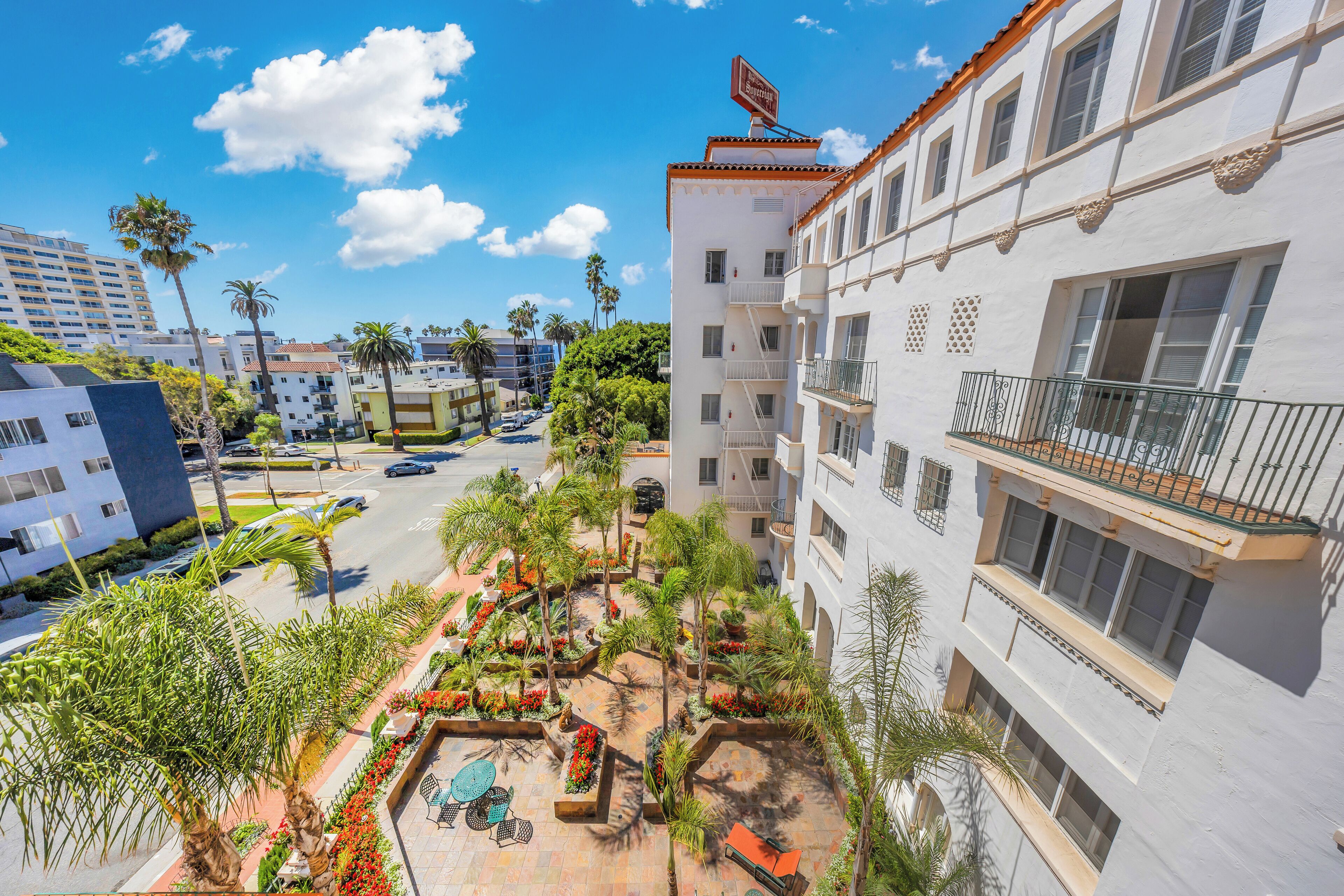 A hotel courtyard with palm trees, outdoor seating, and a pool.