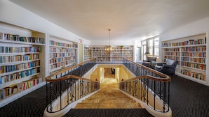 Une bibliothèque spacieuse, dotée de nombreuses étagères, d’un escalier central et d’un lustre.