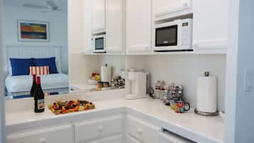 A modern kitchen with white cabinetry, a microwave, a coffee maker, and a breakfast bar with a fruit platter and wine bottles.
