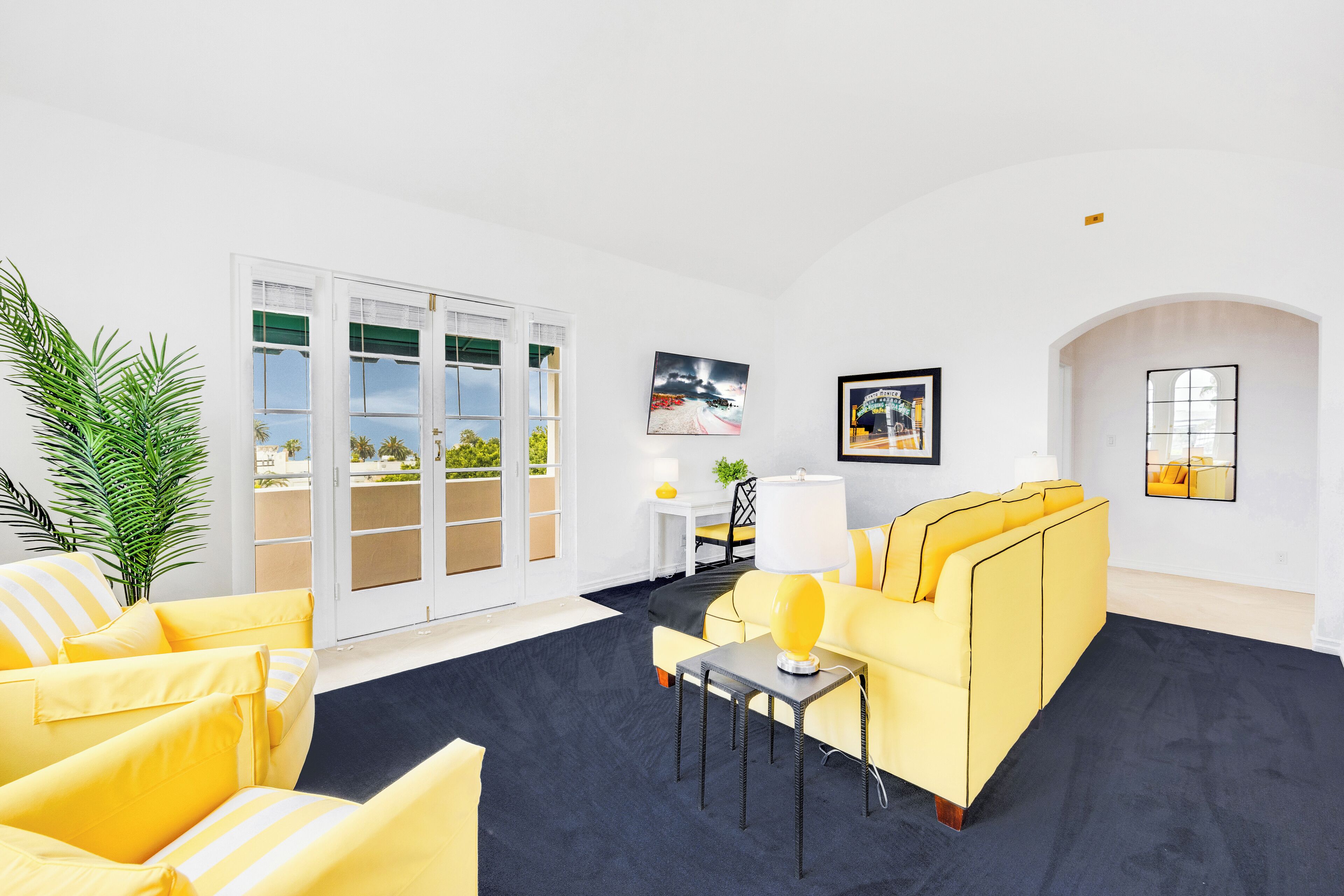 A modern living room with a yellow sofa, a black rug, and a large window with a view of the outdoors.