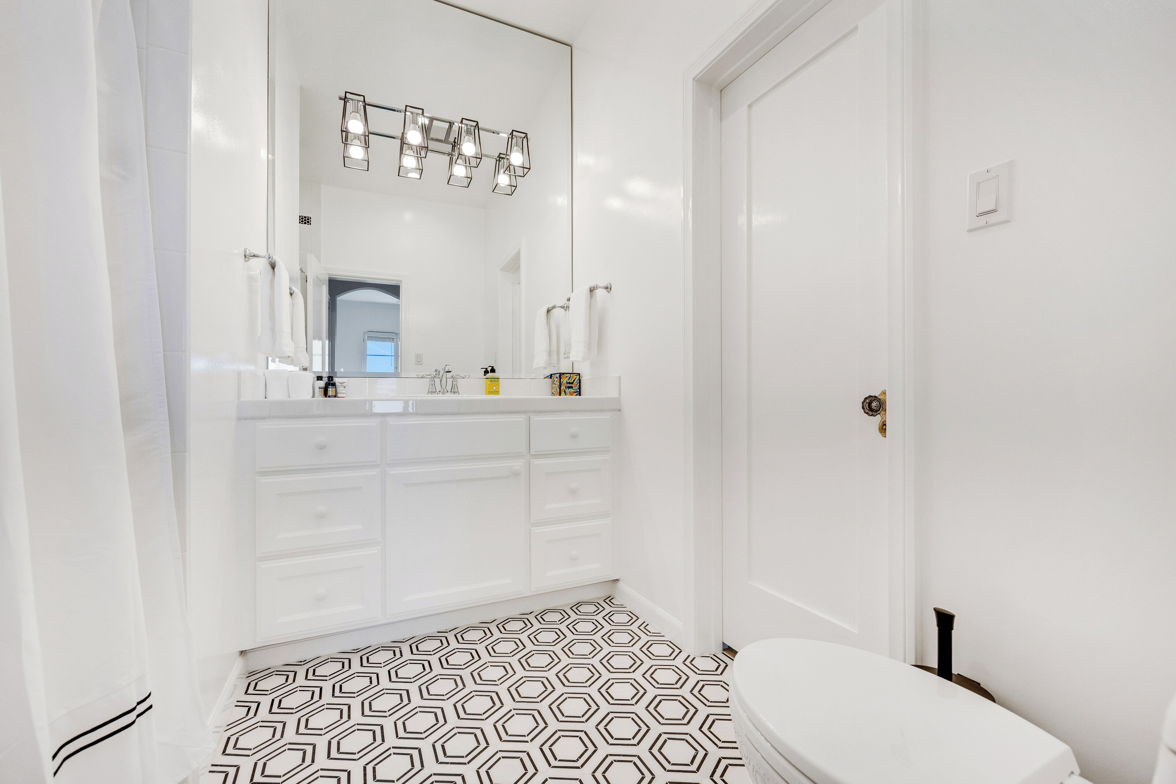 A bathroom with a white vanity, a large mirror, and a black and white patterned floor.