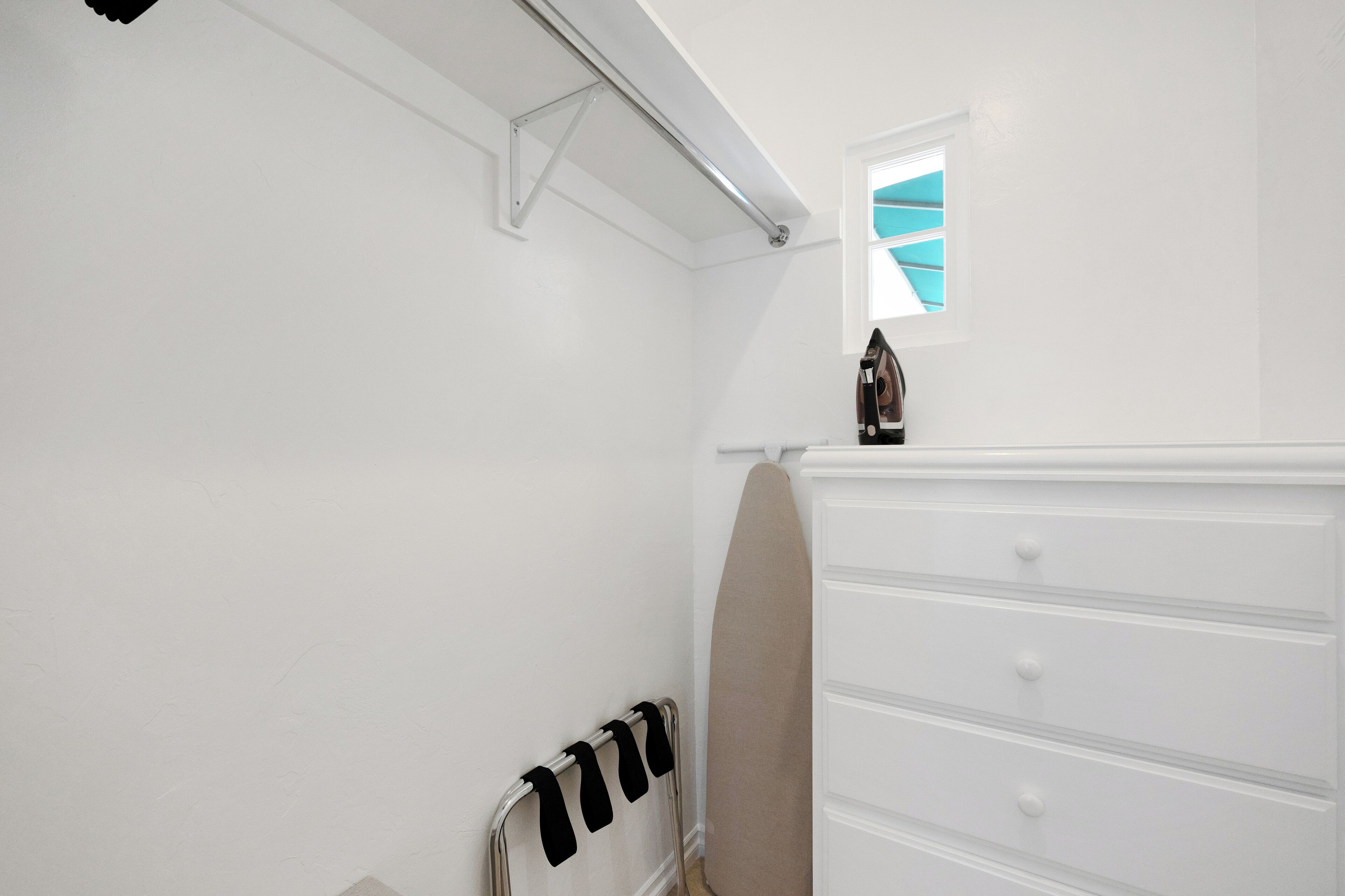 Una habitación blanca con un radiador, un ventanal pequeño y un aparador blanco.