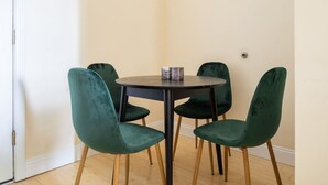 Une table ronde entourée de quatre chaises vertes, un vase en marbre et, au fond, une porte blanche.