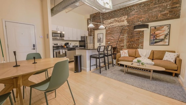 A modern kitchen with stainless steel appliances, a dining area with a wooden table and chairs, and a living space with a sofa and a coffee table. - Simple & Spacious Apartment! (Boston)