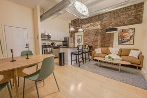 A modern kitchen with stainless steel appliances, a dining area with a wooden table and chairs, and a living space with a sofa and a coffee table. - Simple & Spacious Apartment! (Boston)