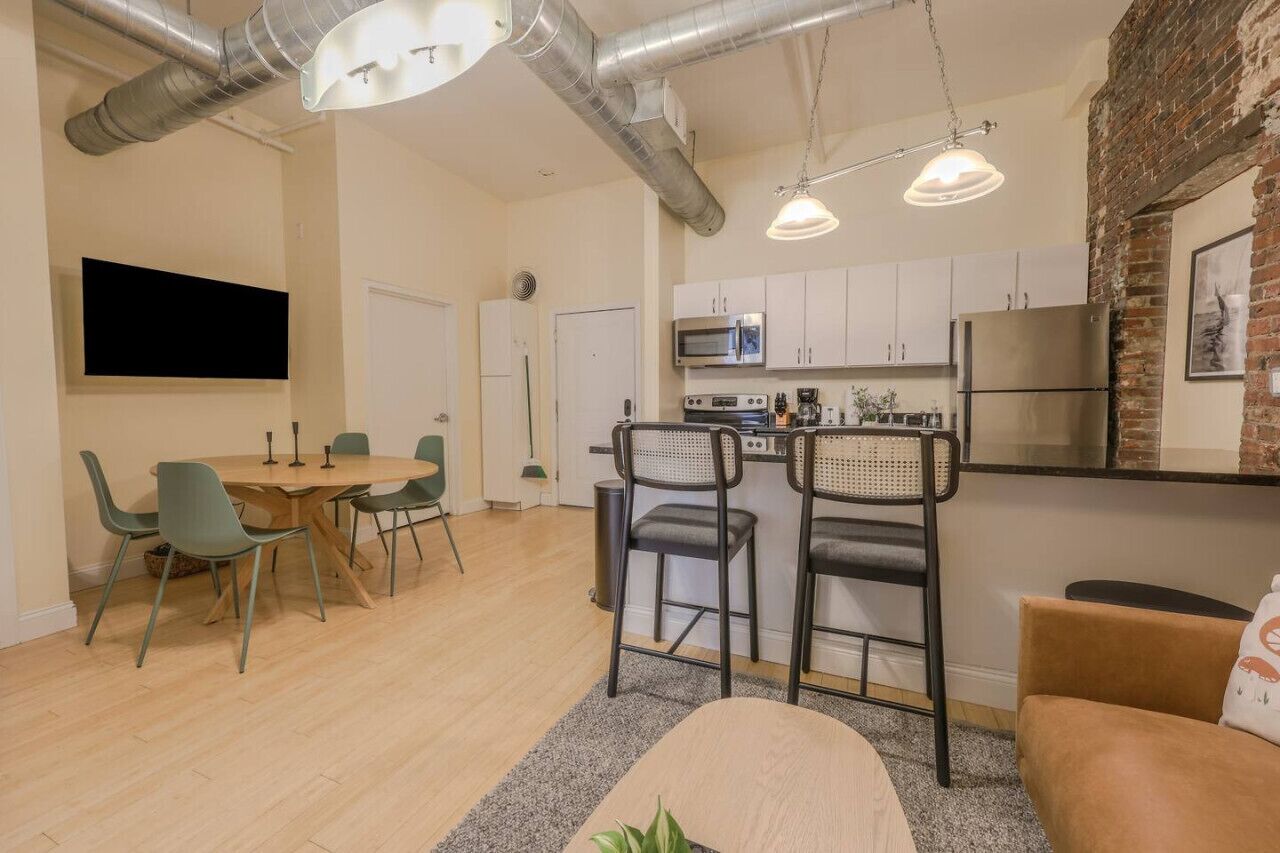 A modern kitchen with stainless steel appliances, a dining area with a round table and chairs, and a cozy seating area with a sofa and a plant.