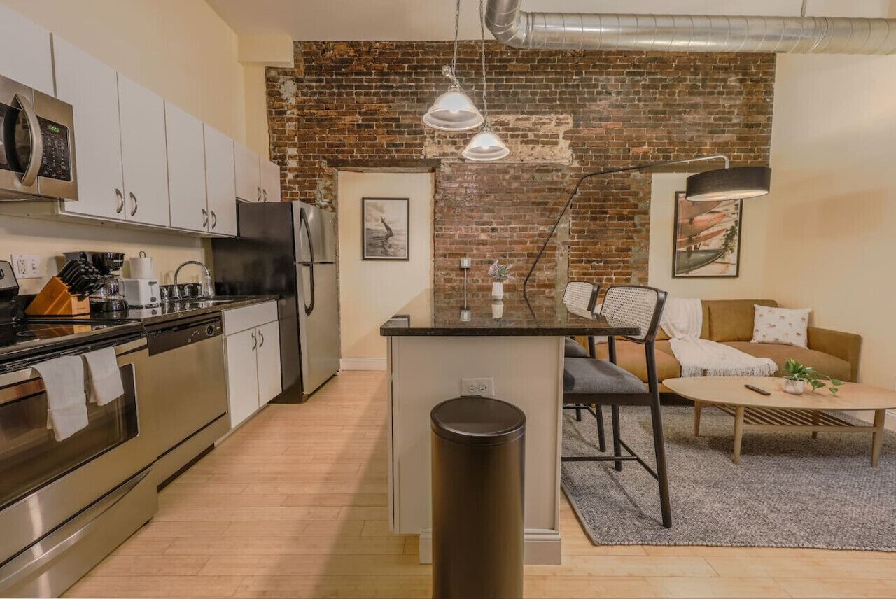 A modern kitchen with stainless steel appliances, a central island, and a brick wall.