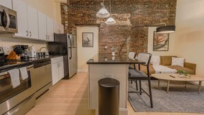 A modern kitchen with stainless steel appliances, a central island, and a brick wall. - Simple & Spacious Apartment! (Boston)