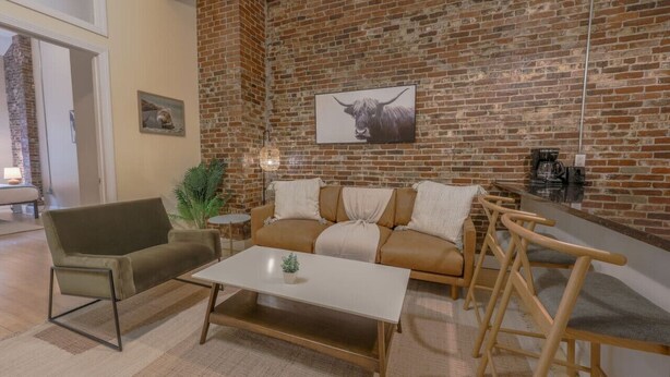 A modern living room with a brick wall, a sofa, a coffee table, and a chair. - Stylish Exposed Brick 3BR! (Boston)