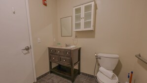 A bathroom with a toilet, a cabinet with drawers, a mirror, and a hand dryer. - Stylish Exposed Brick 3BR! (Boston)