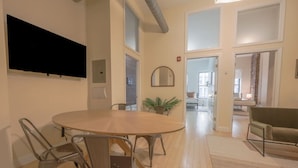 A modern room with a round dining table, metal chairs, a flat-screen TV, a mirror, and a sofa. - Stylish Exposed Brick 3BR! (Boston)