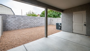 Een overdekt terras met een grindvloer, een betonnen muur en een deur.