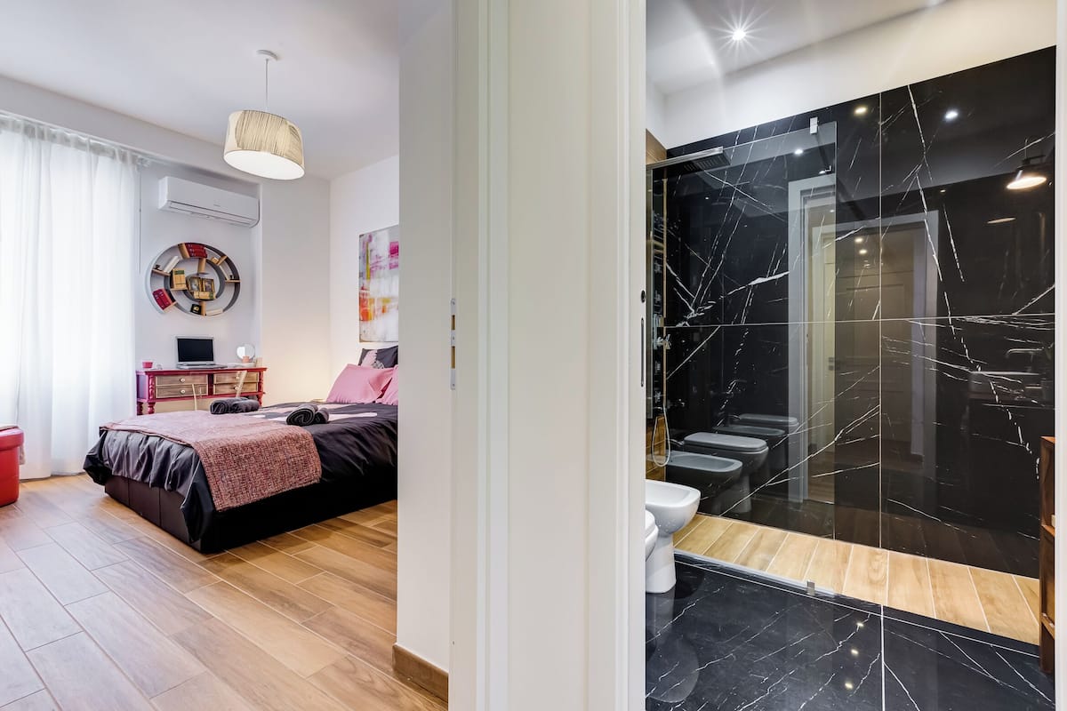 Un dormitorio moderno con cama, mesita de noche y un cubo de basura rojo.