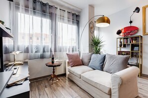 Ein modernes Wohnzimmer mit einer Couch, einem Beistelltisch, einer Lampe, einem Bücherregal und einem Fenster mit durchsichtigen Vorhängen.
