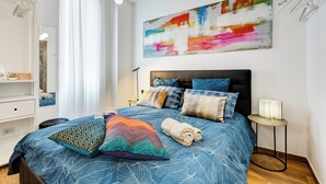 Un dormitorio moderno con una cama grande, un cuadro abstracto lleno de color y una mesita de noche con lámpara.