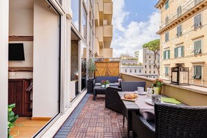 Ein Balkon mit Korbmöbeln, einem Tisch gedeckt mit Tellern, Tassen und einem Brotkorb.