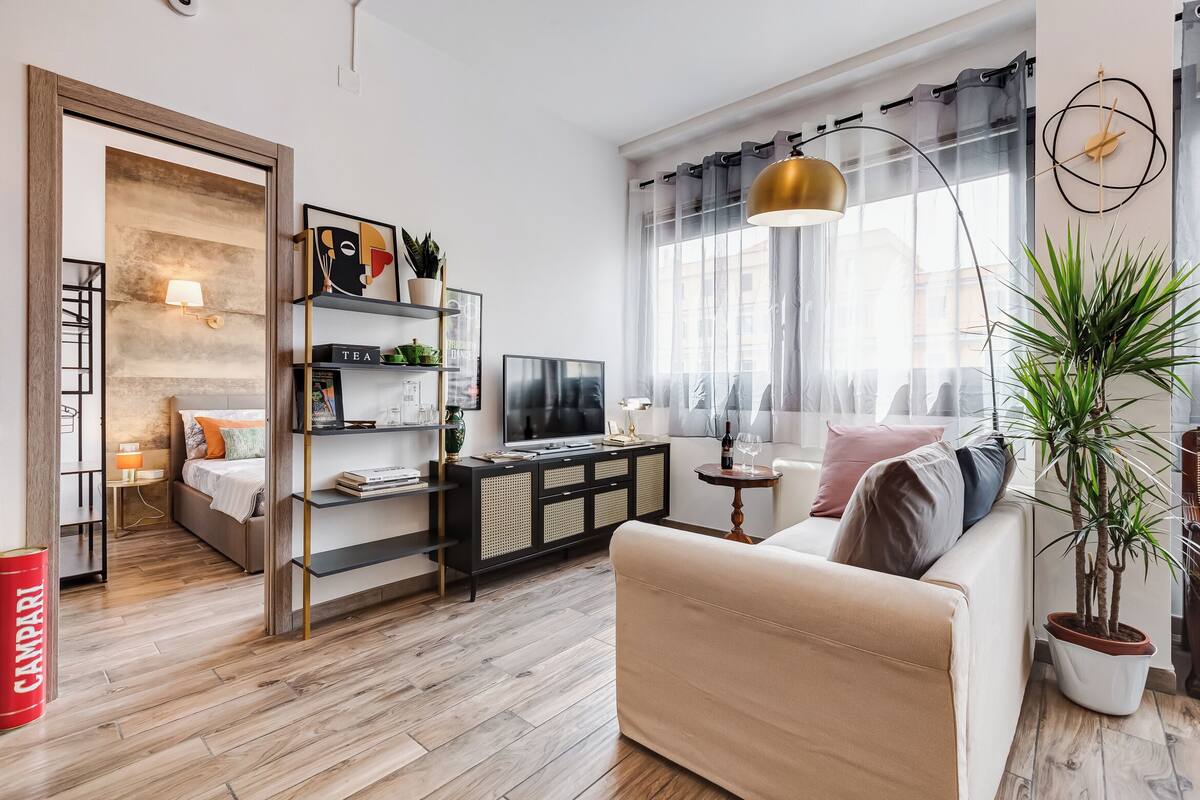 Una sala de estar moderna con un sofá, un televisor, una estantería y un amplio ventanal con cortinas.