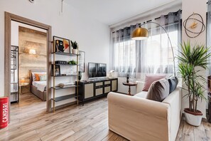 Ein modernes Wohnzimmer mit einer Couch, einem Fernseher, einem Bücherregal und einem großen Fenster mit Vorhängen.