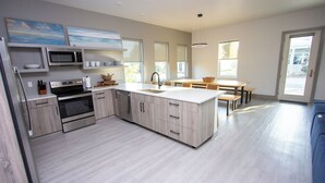 A modern kitchen with built-in appliances, a dining area with a table and chairs, and a large window providing natural light. - Firefly South: 3,800 sqft - Sleeps 16! 2-min walk to pool and beach! (Saint Teresa)