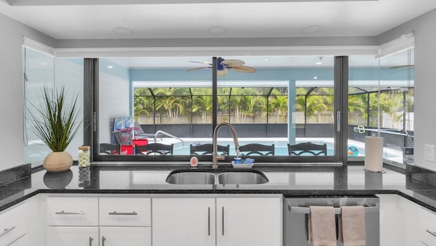 Una cocina moderna con un ventanal grande, un ventilador de techo y vistas a una piscina y palmeras.
