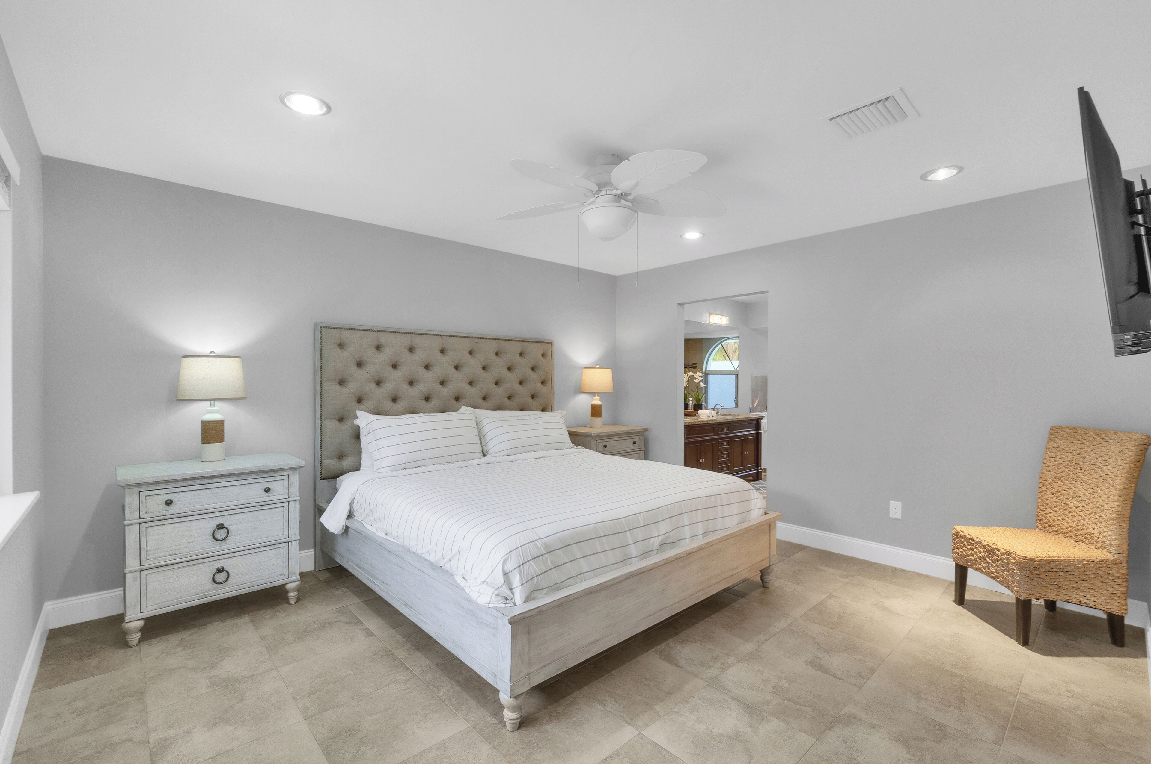 A bedroom with a large bed, two bedside tables, a ceiling fan, and a chair.