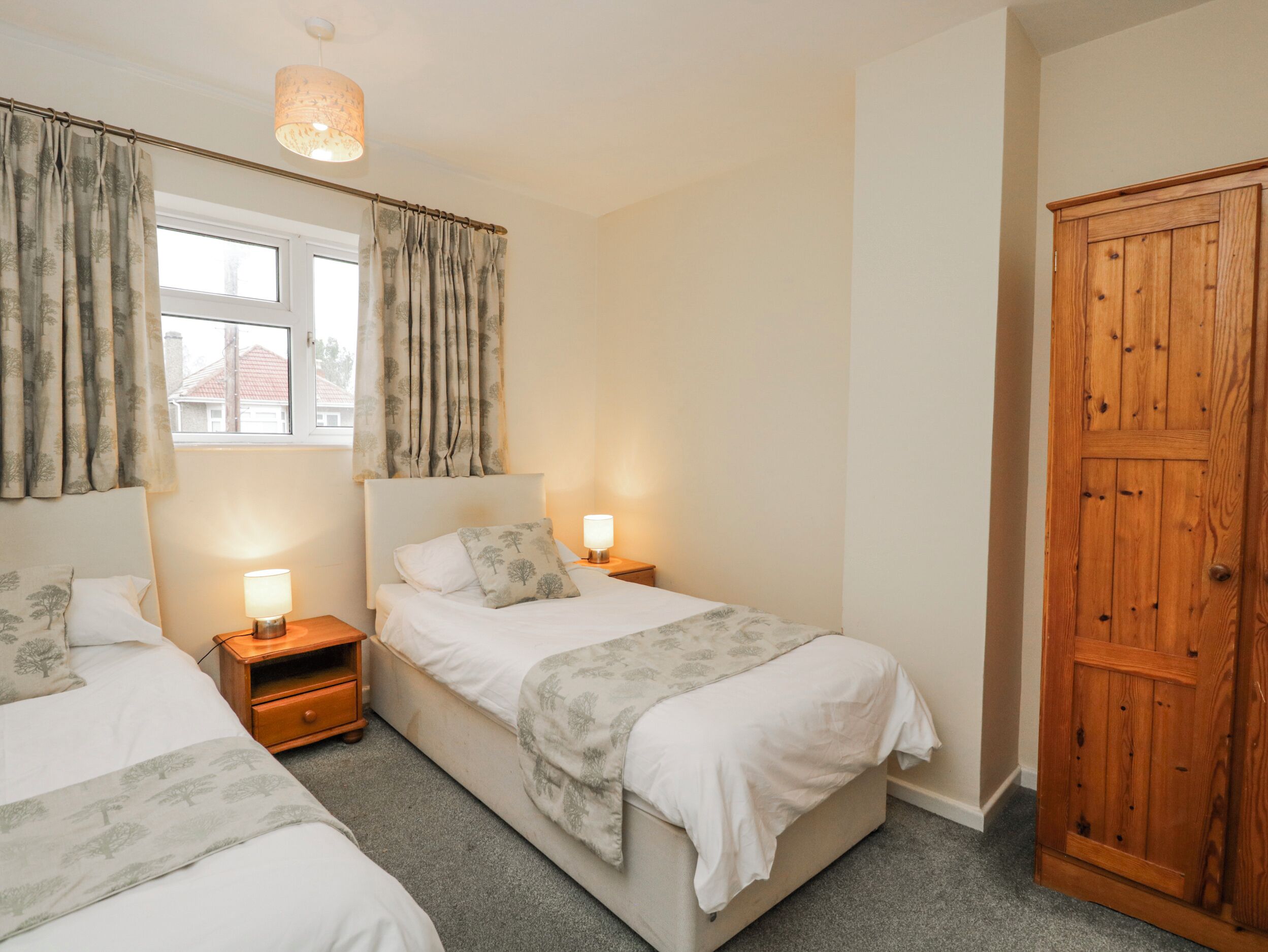 A bedroom with two beds, a wooden wardrobe, and a window with curtains.