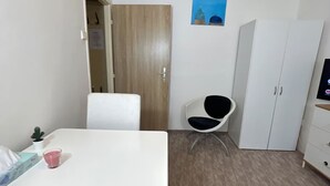 Et lille, pænt møbleret værelse med et hvidt bord, en sort stol, et hvidt skab og en dør, der fører til et andet værelse.