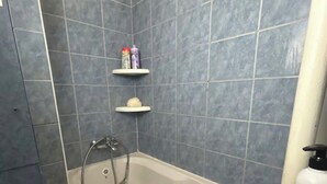 Et badeværelse med badekar, vask og toilet. To hylder med toiletartikler.