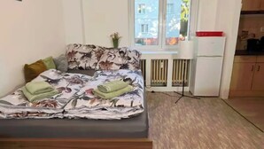 Et værelse med en seng, et lille skrivebord, et vindue og et tekøkken.
