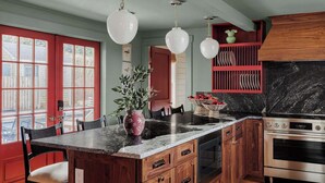 Et køkken med marmor bordplade, træskabe, en rød dør og en backsplash i sort marmor.