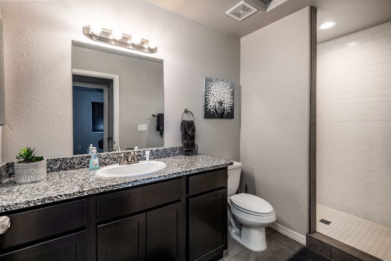 A modern bathroom with a granite countertop, dual sinks, a large mirror, and a toilet.