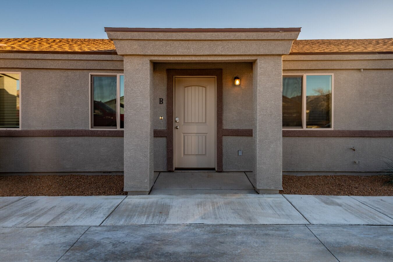 A single-story building with a beige exterior, a front door with a small overhang, and a single window on each side.