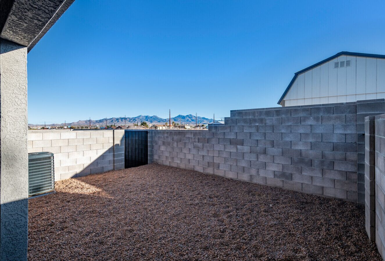 A covered outdoor area with a gravel floor, surrounded by walls and a building in the background.