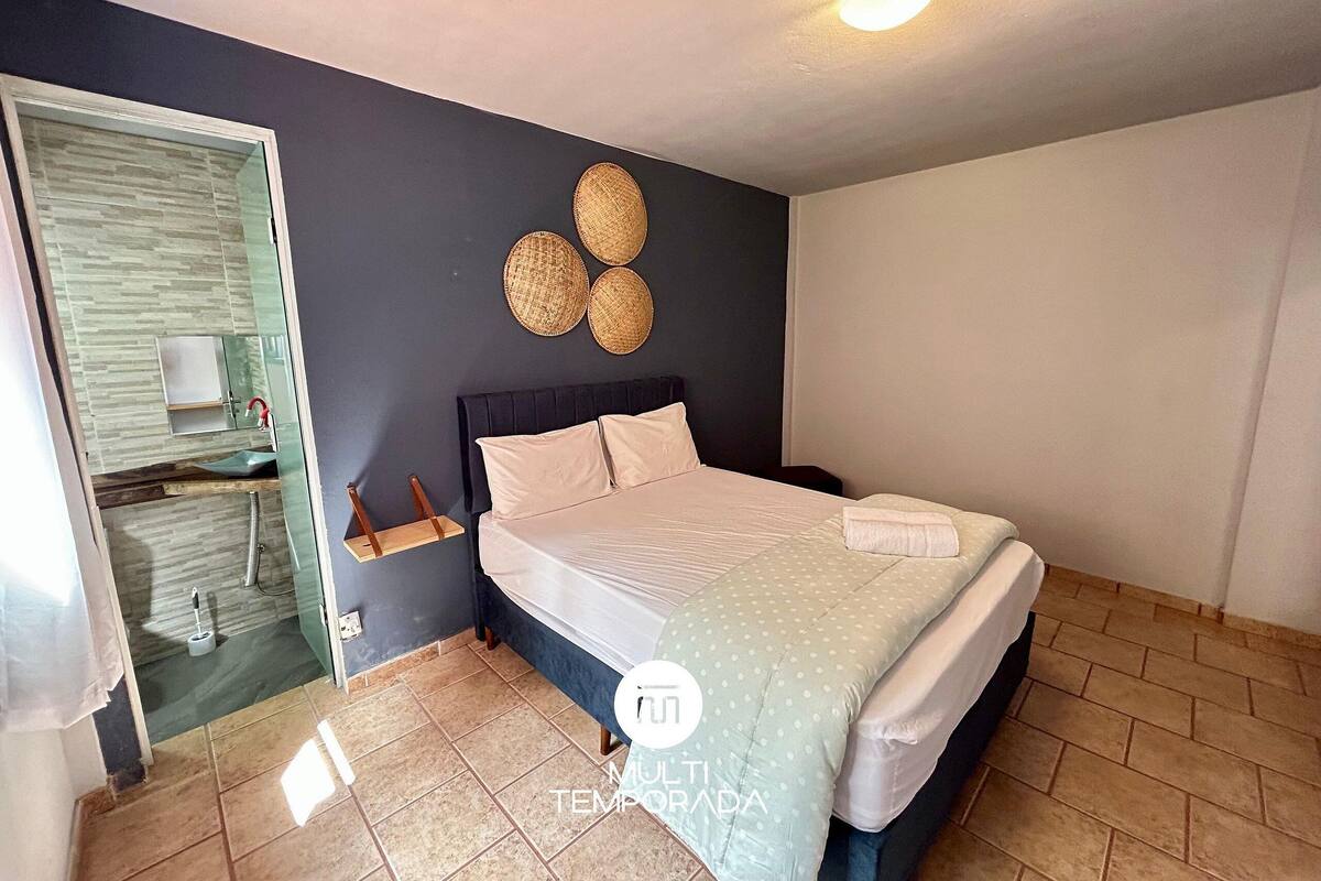A bedroom with a bed, a bedside table, a mirror, and a wall-mounted light fixture.