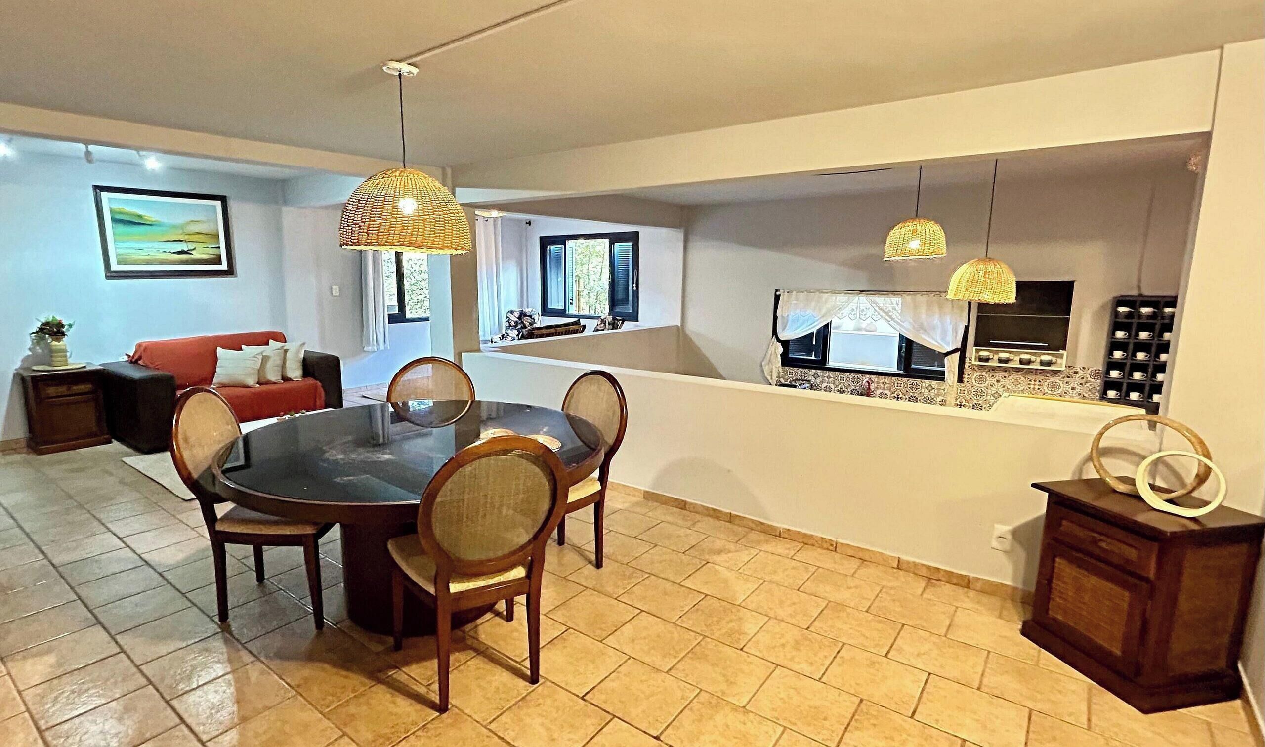 A dining area with a round table and chairs, a red sofa, and a kitchen area with a window and a shelf with cups.