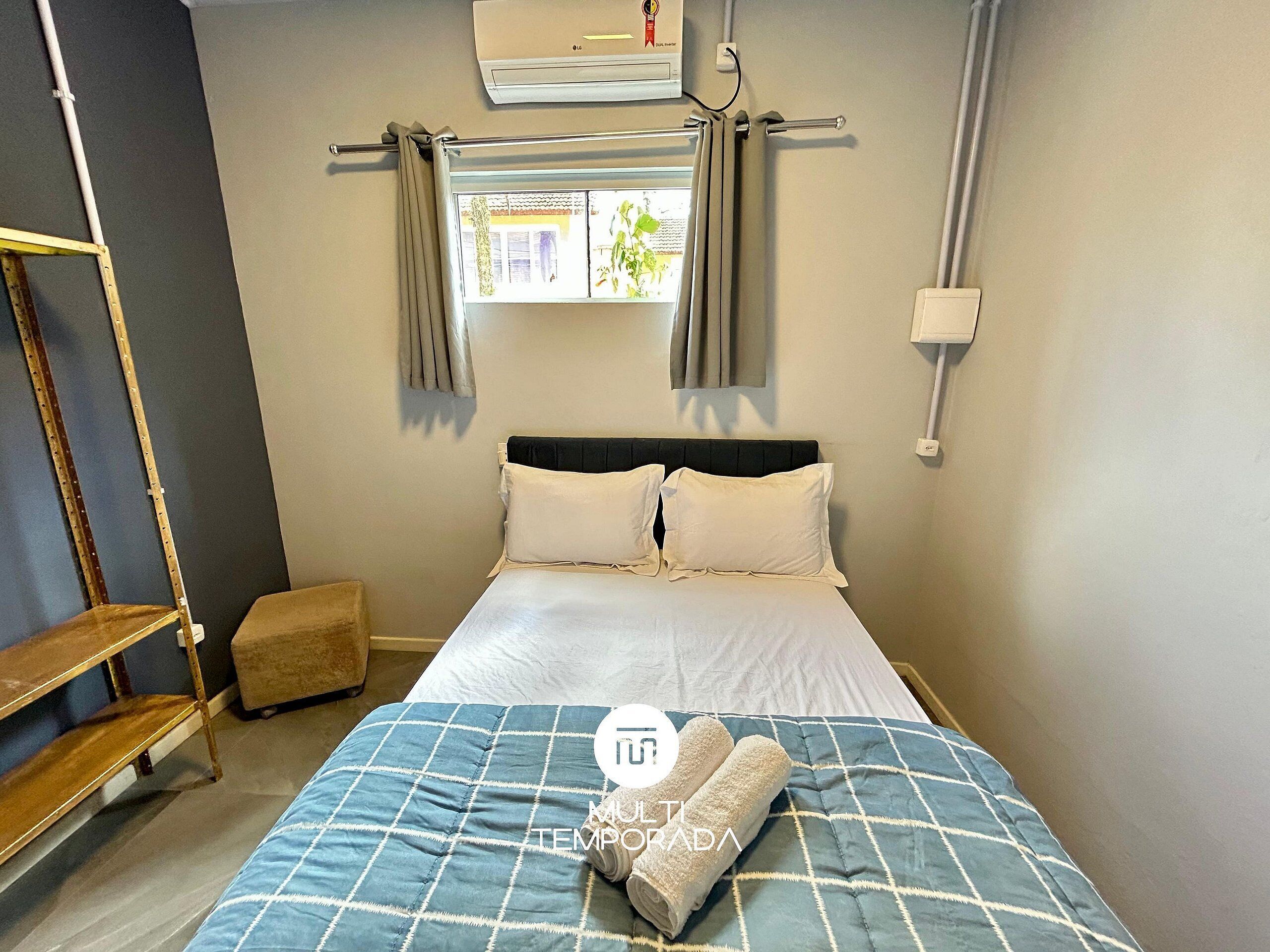 A bedroom with a bed, a window with curtains, a wooden ladder, and a wall-mounted air conditioner.