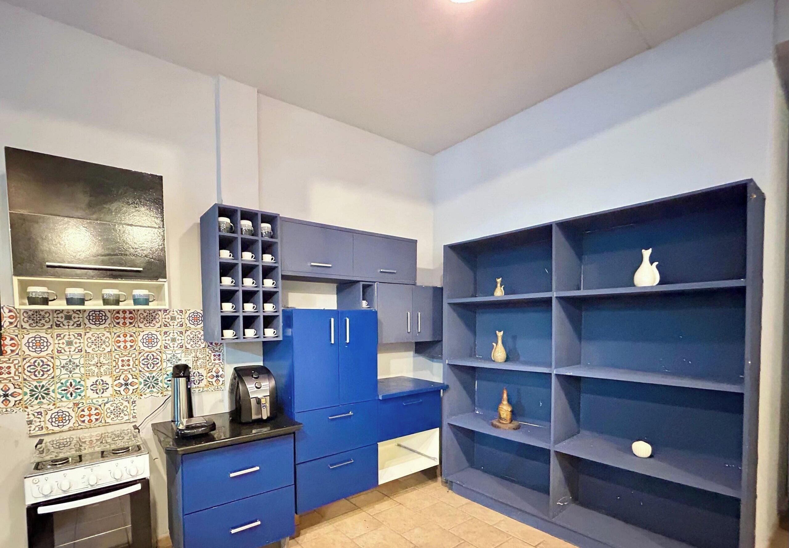 A compact kitchen with blue cabinets, a coffee machine, and a tiled backsplash.