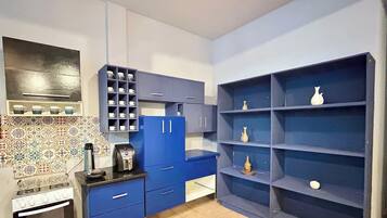A compact kitchen with blue cabinets, a coffee machine, and a tiled backsplash.