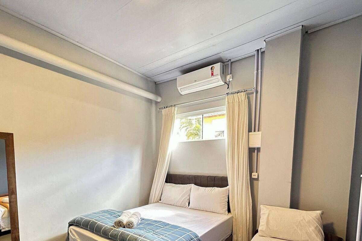 A bedroom with a bed, a window with curtains, an air conditioning unit, and a mirror.