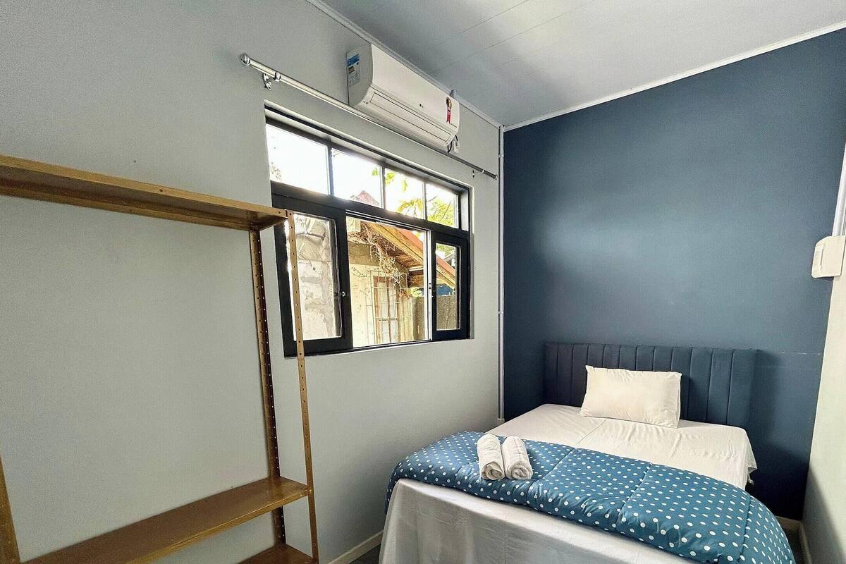 A small, single-bed room with a window, a wooden shelf, and a bed with a polka dot cover.