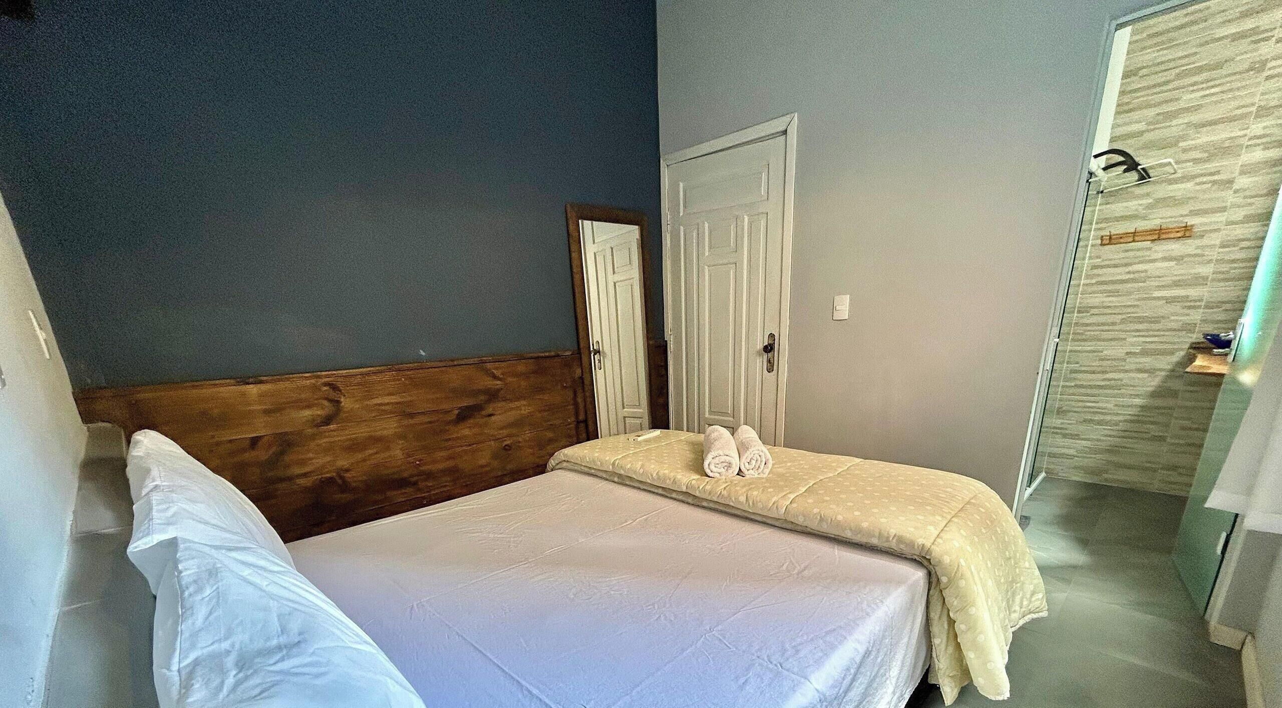 Un dormitorio con cabecera de madera, una cama con colchón blanco y manta color beige, y una mesita de noche con toallas.