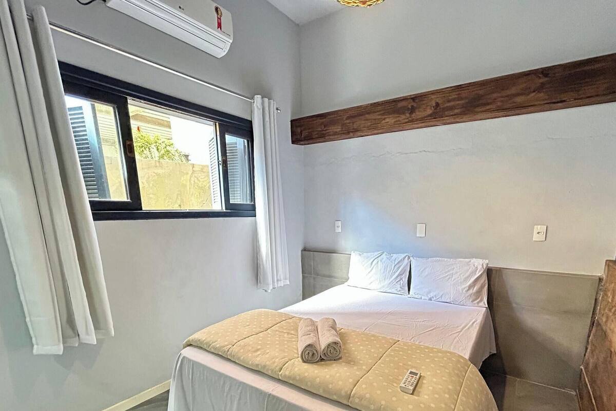 A bedroom with a bed, a window with curtains, a wooden beam on the wall, and a ceiling fan.